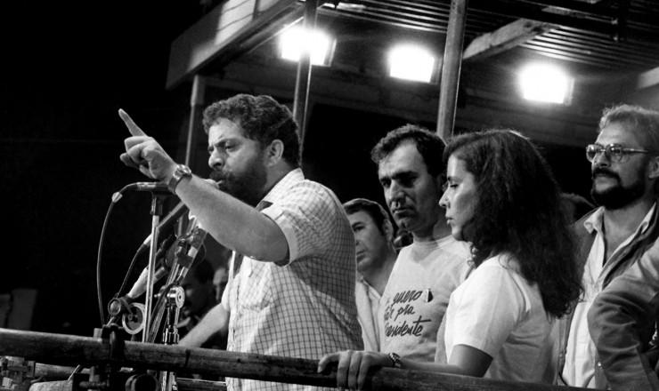  <strong> Lula no palanque da Candelária, </strong> observado pelo narrador Osmar Santos (atrás) e o ator José Wilker (ao fundo) 