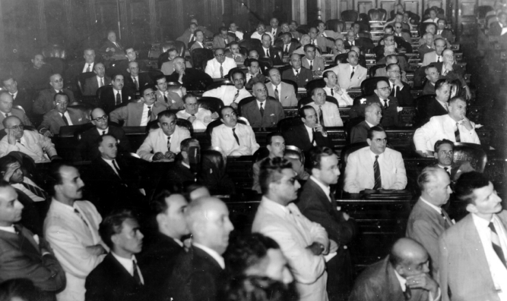  <strong> Vista parcial do plenário </strong> da Assembleia Nacional Constituinte de 1946. Da esquerda para a direita, segunda fila: Gustavo Capanema (2º), José Maria Alckmin (5º), José Francisco Bias Fortes (6º). Na terceira fila: Agamenon Magalhães (7º) e Benedito Valadares (8º)   