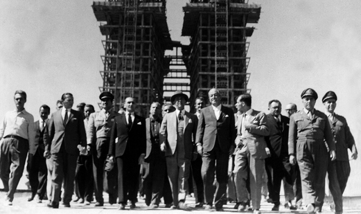  <strong> De chapéu, o presidente Juscelino caminha</strong> com assessores e correligionários nas obras da futura capital, tendo ao fundo as torres do Congresso Nacional. Brasília, 1959